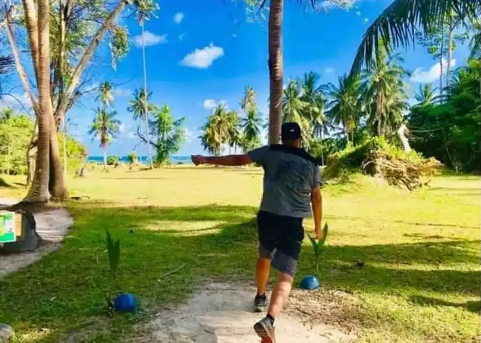 A player drives under a bright blue sky with palms and the sea behind