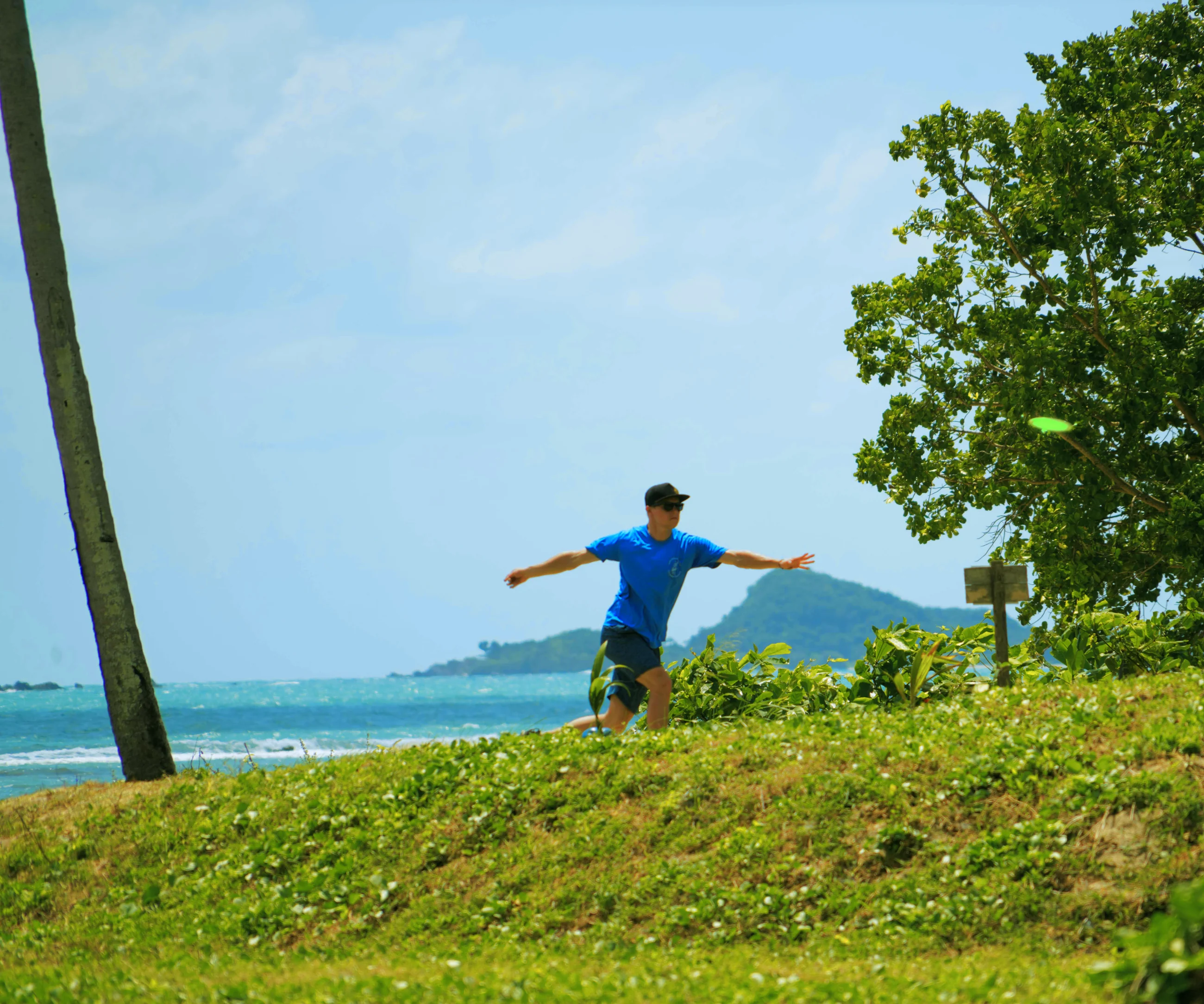 A player throws on the grassy bank above the sea, with an island behind, at Disc Golf Thailand, Koh Samui