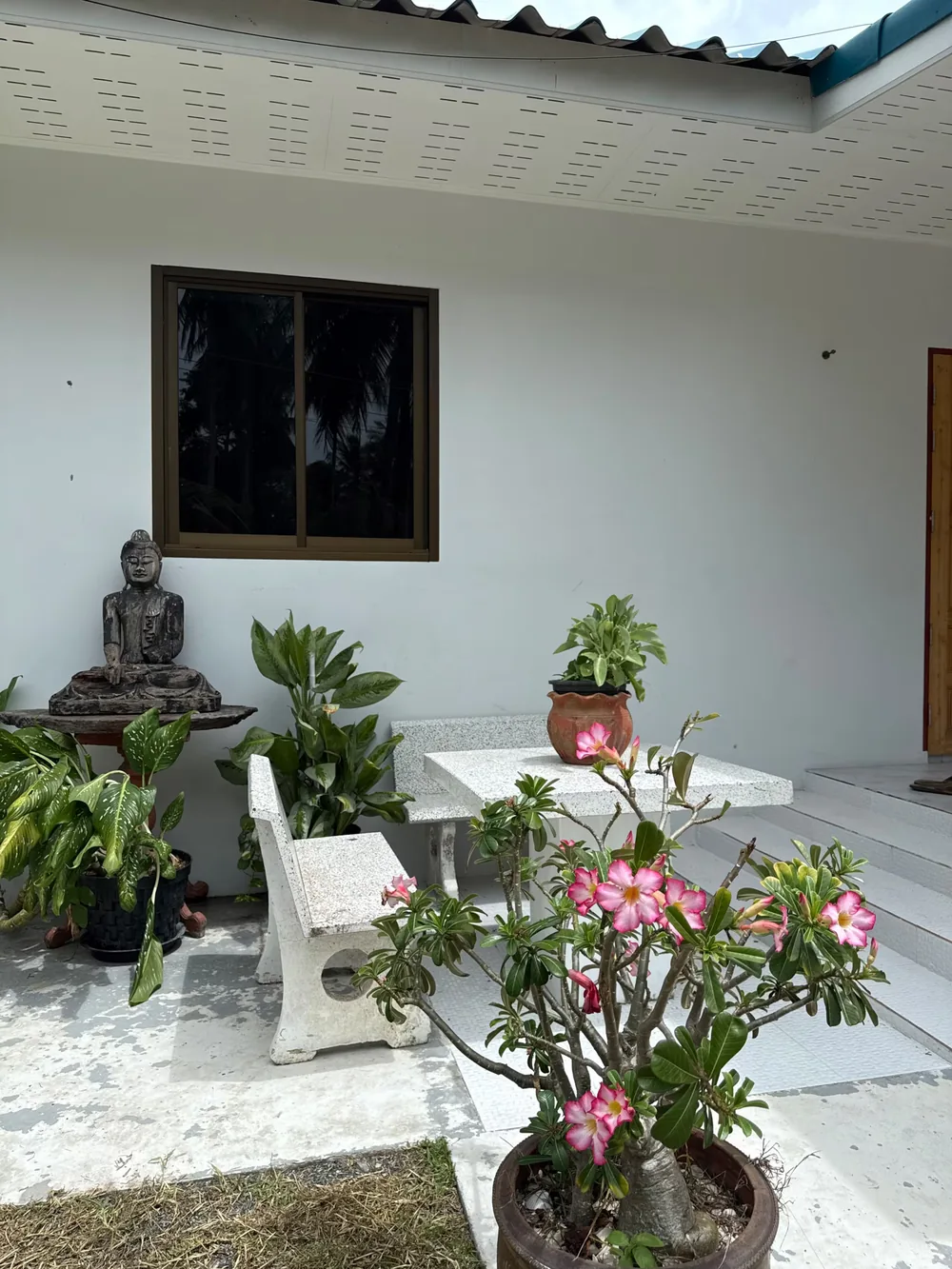 The guesthouse patio with a stone table, potted plants and a Buddha statue